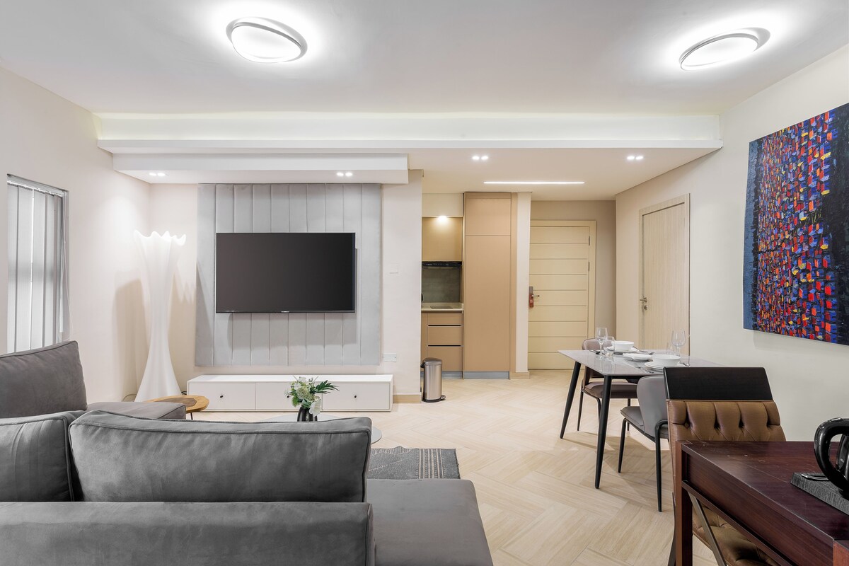 Una sala de estar moderna con un sofá gris, un televisor de pantalla plana y un comedor con una mesa y sillas de madera.