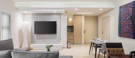 A modern living room with a grey sofa, a flat-screen TV, and a dining area with a wooden table and chairs.