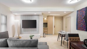 A modern living room with a grey sofa, a flat-screen TV, and a dining area with a wooden table and chairs. - DOMO by Design Union (Lekki)