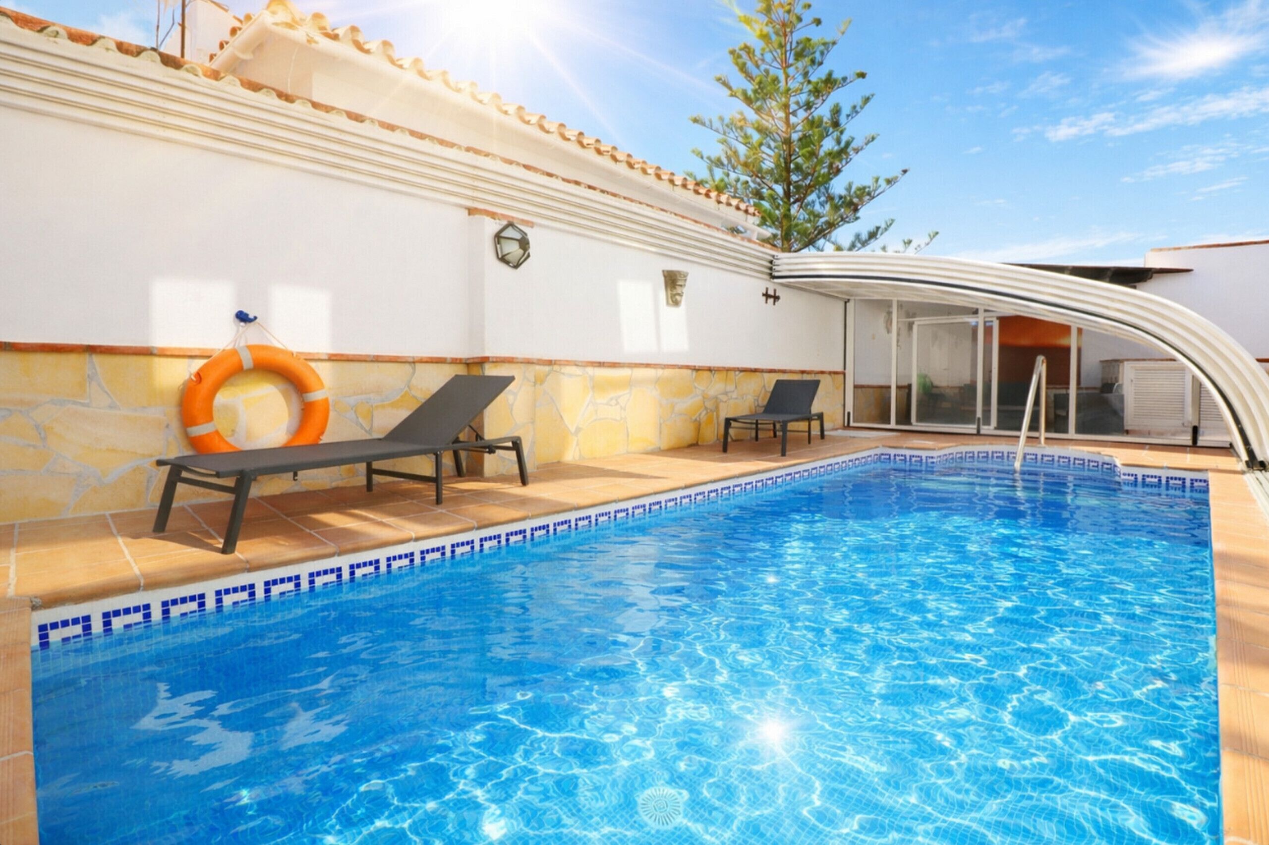 Una piscina amb dues gandules, un salvavides i una porta de vidre que dona a una zona coberta.