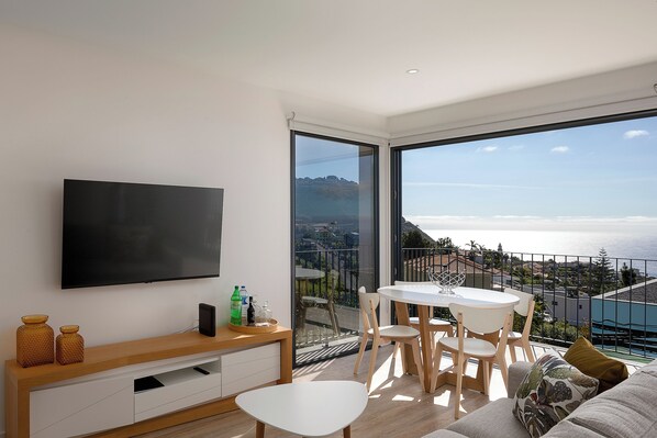 A modern living room with a flat-screen TV, wooden furniture, and a balcony with a view of the sea. - MARCO 4 SEASONS - FALL (Arco da Calheta)