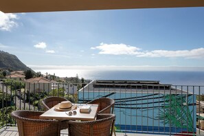 Ein Balkon mit Korbmöbeln, einem Tisch mit Hut und Buch, und Blick auf das Meer und Gebäude.