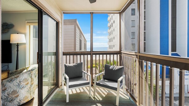 Ein Balkon mit zwei weißen Stühlen, einer Couch und Blick auf ein gegenüberliegendes Gebäude.