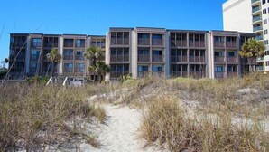 Ein Strandhotel mit mehrstöckigen Gebäuden, einem Sandweg zum Eingang und einigen Palmen.