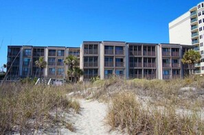 Ein Strandhotel mit mehrstöckigen Gebäuden, einem Sandweg zum Eingang und einigen Palmen.