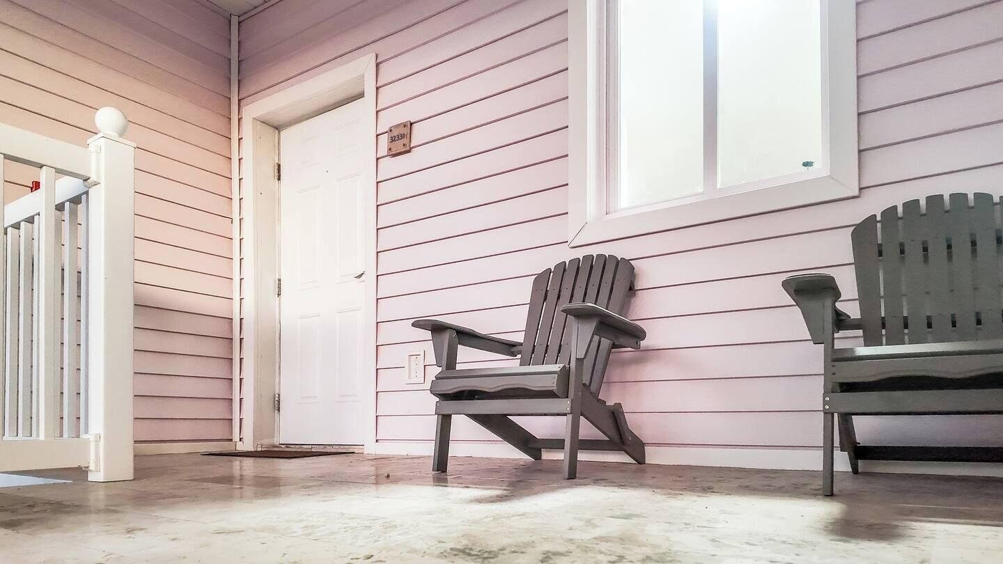 Een veranda met twee Adirondack-stoelen, een witte deur en een raam.
