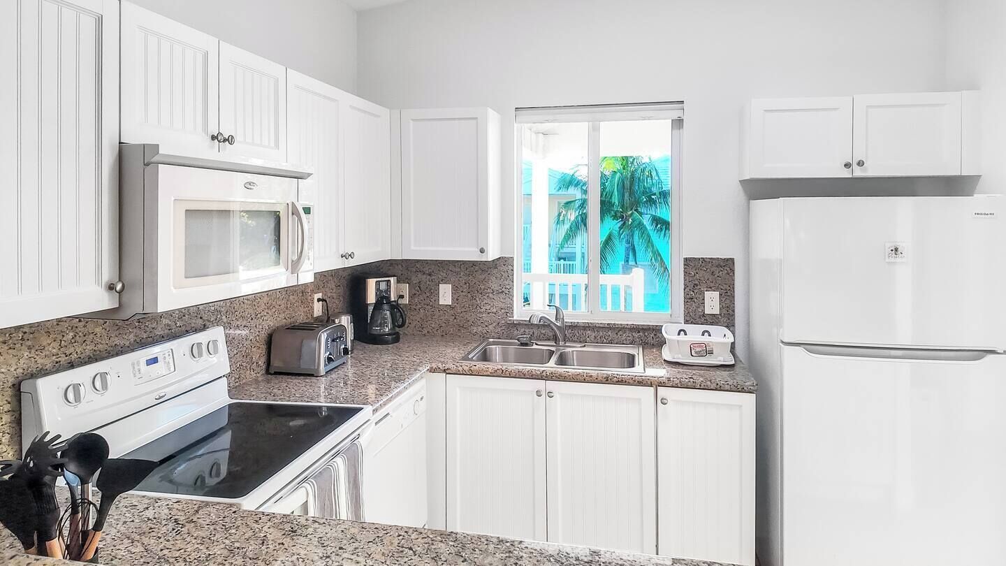 A kitchen with white cabinets, a microwave, a stove, a sink, and a refrigerator.
