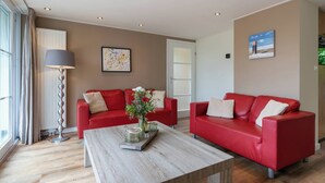 Un saló modern amb dos sofàs vermells, una taula de centre de fusta i una làmpada de peu.
