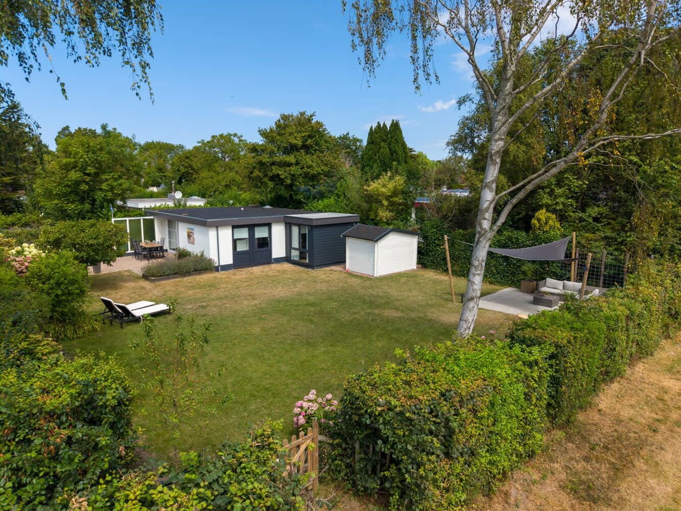 Ein modernes Haus mit gepflegtem Rasen, einer Terrassenanlage und einem kleinen Schuppen.