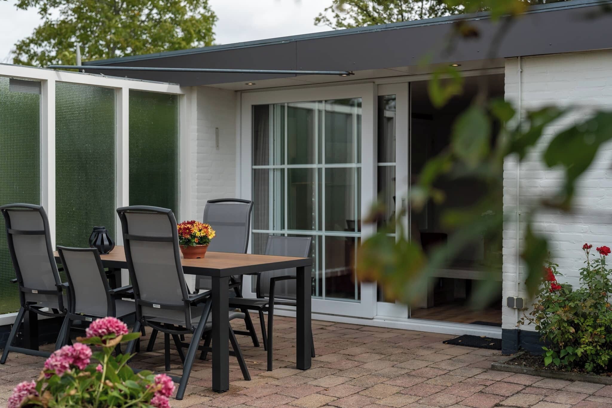 An outdoor patio with a table and chairs, a potted plant, and a sliding glass door leading to a covered area.
