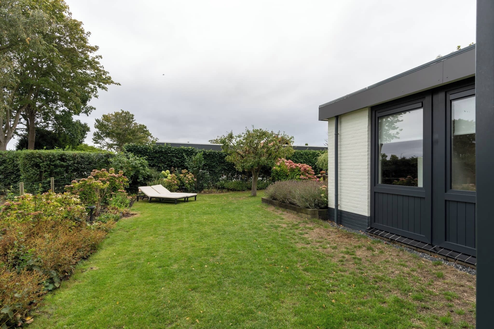 A modern house with a well-maintained garden, a lounge chair, and a large window.