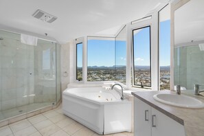 A modern bathroom with a large bathtub, a glass-enclosed shower, and a view of a cityscape through large windows. - Elysian Blue 3BR Burleigh Heads Escape (Burleigh Heads)