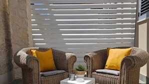 Un patio con mobiliario de mimbre, una mesa blanca y una estructura de listones blancos al fondo.