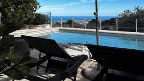 Ein Poolbereich mit Liegestühlen und Sonnenschirmen, mit Blick auf einen klaren, blauen Himmel und eine ferne Meerlandschaft.