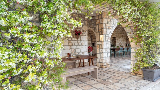 Eine Terrasse im Freien mit steinernen Bögen, einem Holztisch und Bänken.