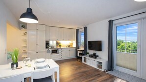 Una cucina moderna con mobili bianchi, una zona pranzo con tavolo e sedie, una TV a parete e un balcone con vista.