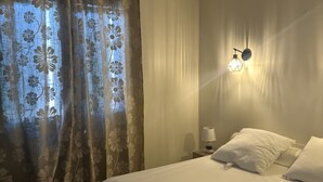 A bedroom with a bed, curtains, a wall-mounted light, and a nightstand. - Holiday Home "La Maison De Campagne" with Mountain View, Private Terrace and Garden (Salles-Curan)