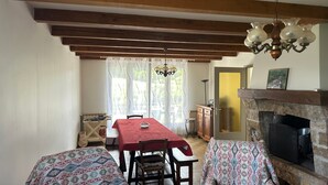 A dining area with a table and chairs, a fireplace, and a view through a window with curtains. - Holiday Home "La Maison De Campagne" with Mountain View, Private Terrace and Garden (Salles-Curan)
