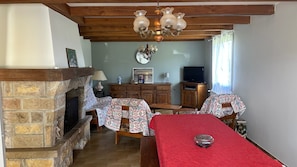 Ein gemütliches Wohnzimmer mit Kamin, Holzbalken, einem Esstisch und einem Fernseher.