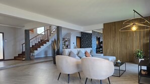 A spacious living area with a modern staircase, a sofa set, and a hanging light fixture. - Casa do Mundo Madeira (Santa Cruz)