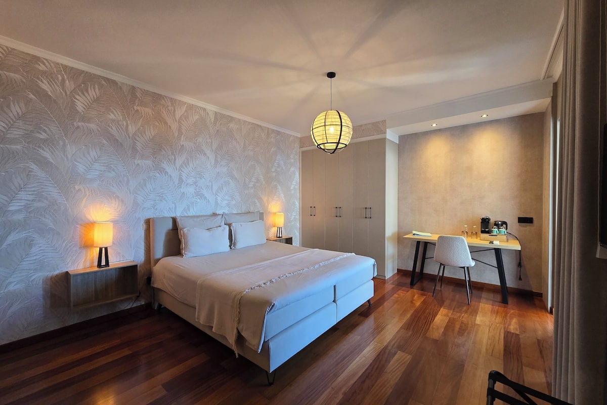 Un dormitorio moderno con una cama grande, lámparas de noche, un escritorio con una silla y una lámpara de techo.