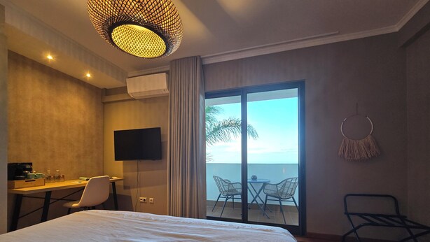 A hotel room with a bed, a desk with a TV, a chair, a balcony with a view of the sea, and a hanging decoration. - Casa do Mundo Madeira (Santa Cruz)