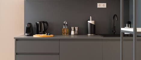 Una cocina moderna con armarios grises, encimera de madera, cafetera, hervidor, salero y grifo negro.