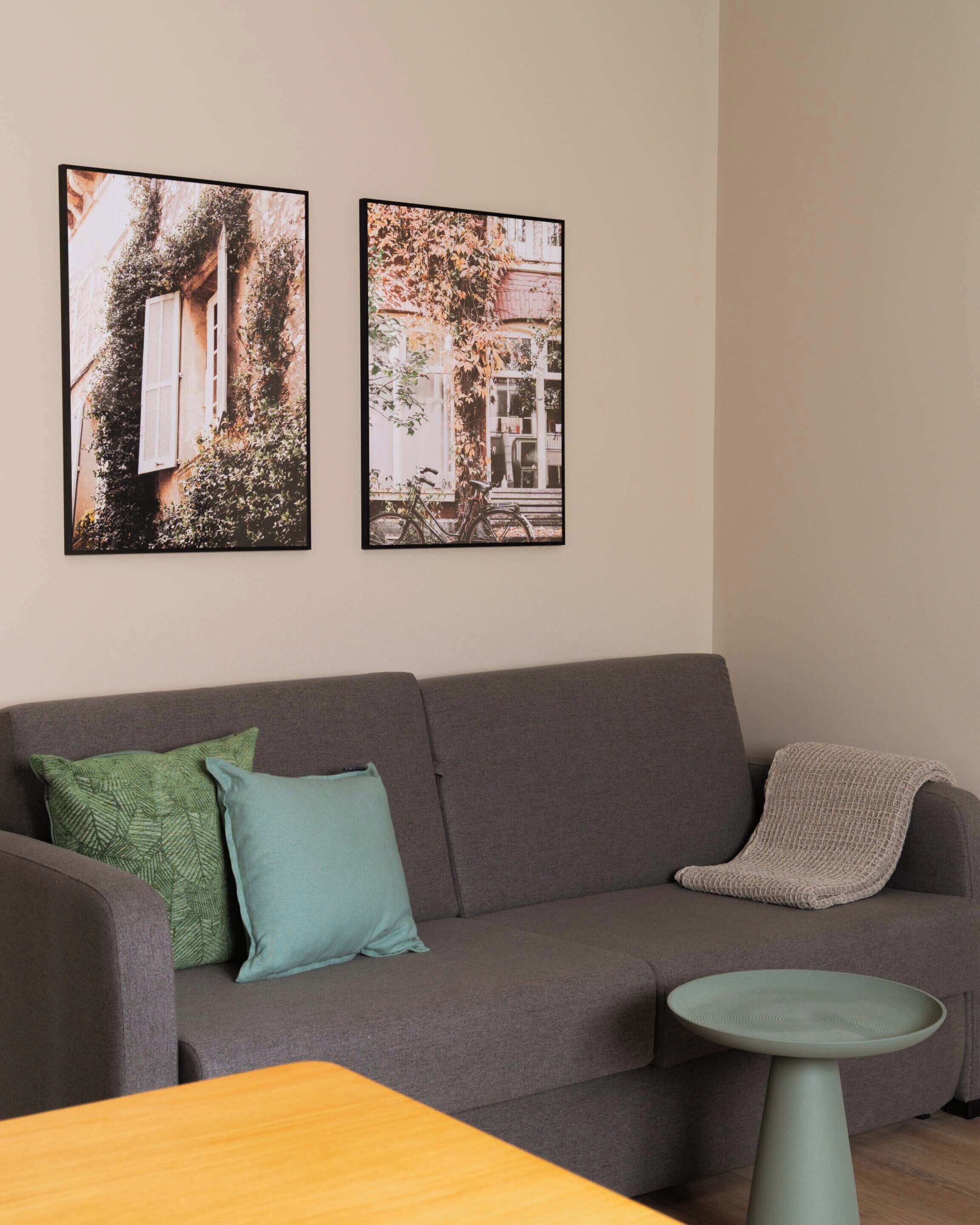 A living room with a grey sofa, two cushions, a small round table, and two framed pictures on the wall.