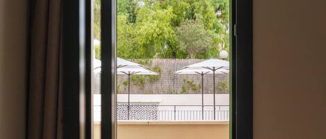Puerta abierta que da a un patio exterior con una mesa y sillas, rodeado de follaje y sombrillas.