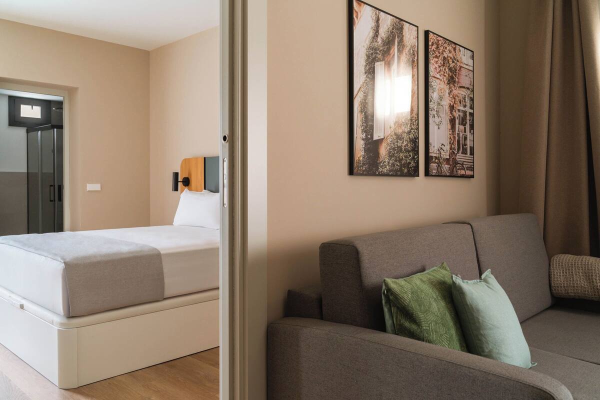 A modern hotel room with a bed, a sofa, and two framed pictures on the wall.