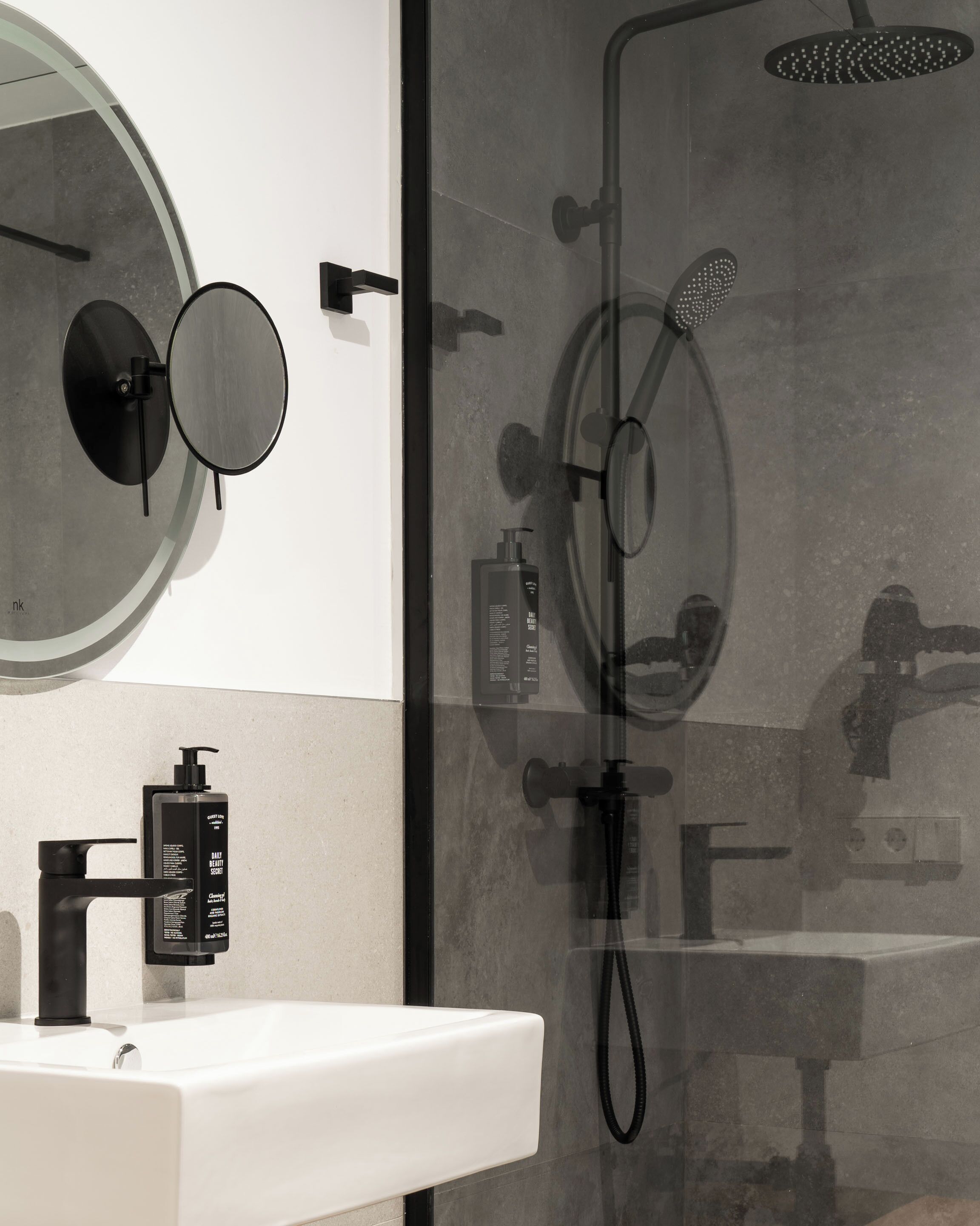 A modern bathroom with a white sink, black fixtures, a round mirror, and a glass-enclosed shower area.