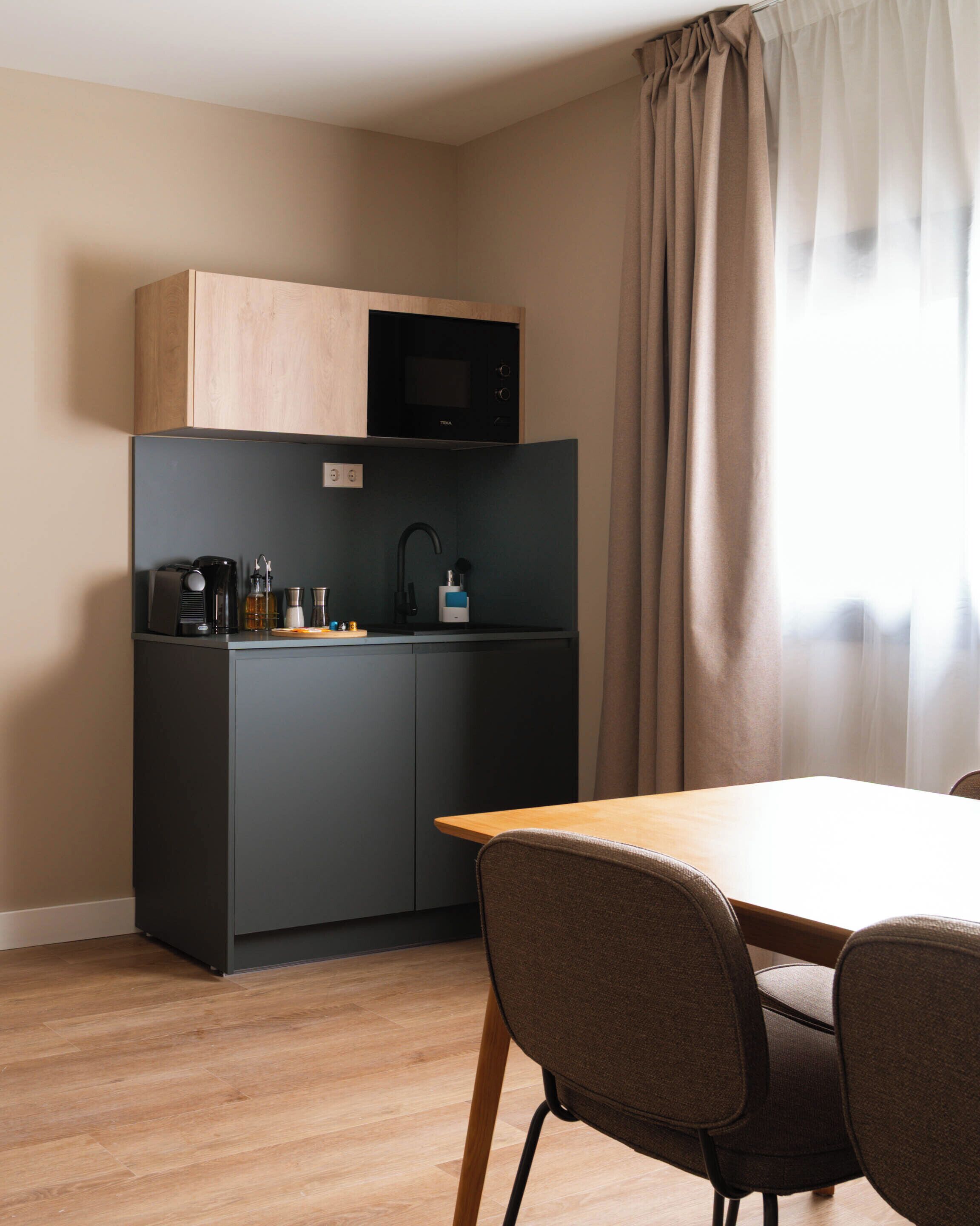 A compact kitchenette with a microwave, coffee maker, and sink. There is a dining table with chairs in front.