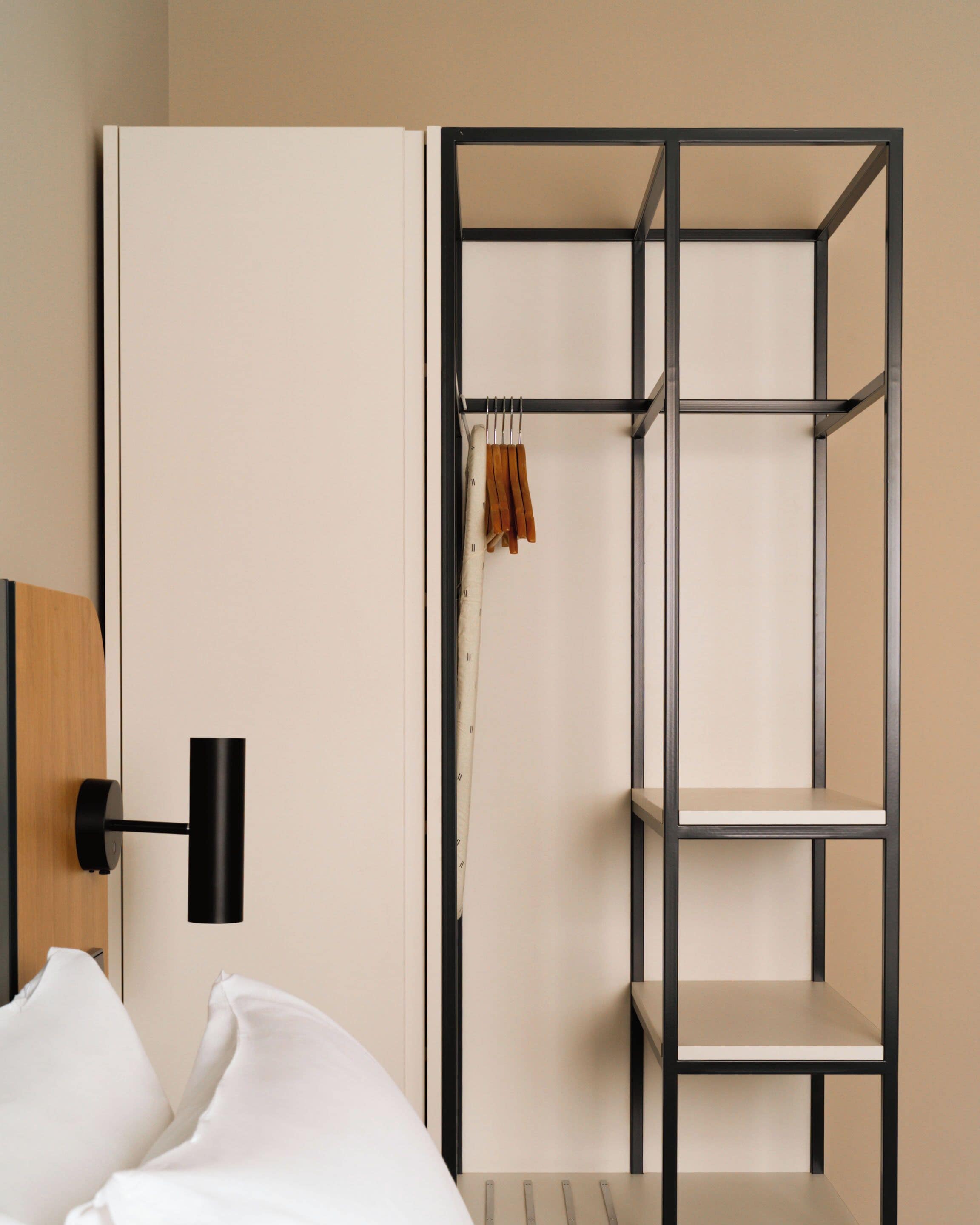 A minimalist room with a bed, a wall-mounted shelf, and a wardrobe with a hanging rack.