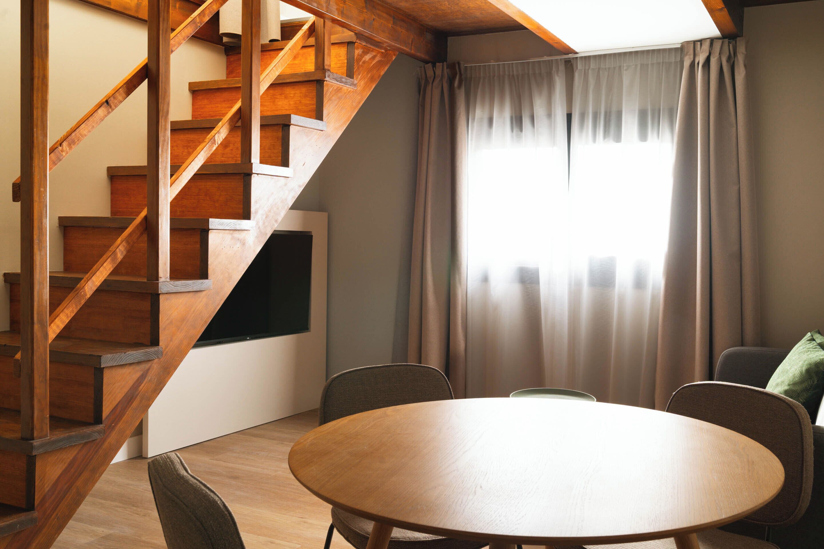 Un salon moderne avec un escalier en bois, une table ronde en bois et un coin salon confortable.