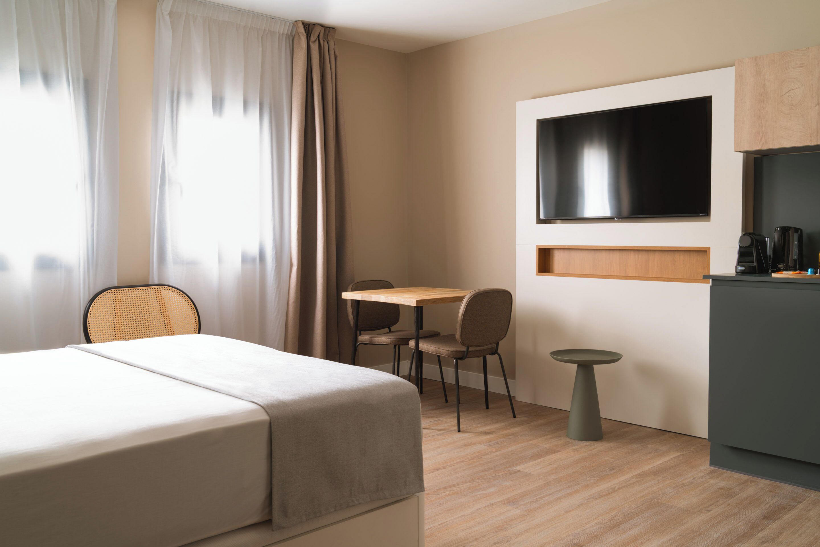 Een hotelkamer met een bed, een eettafel met stoelen, een klein rond tafeltje, een aan de muur bevestigde televisie, en een kitchenette.