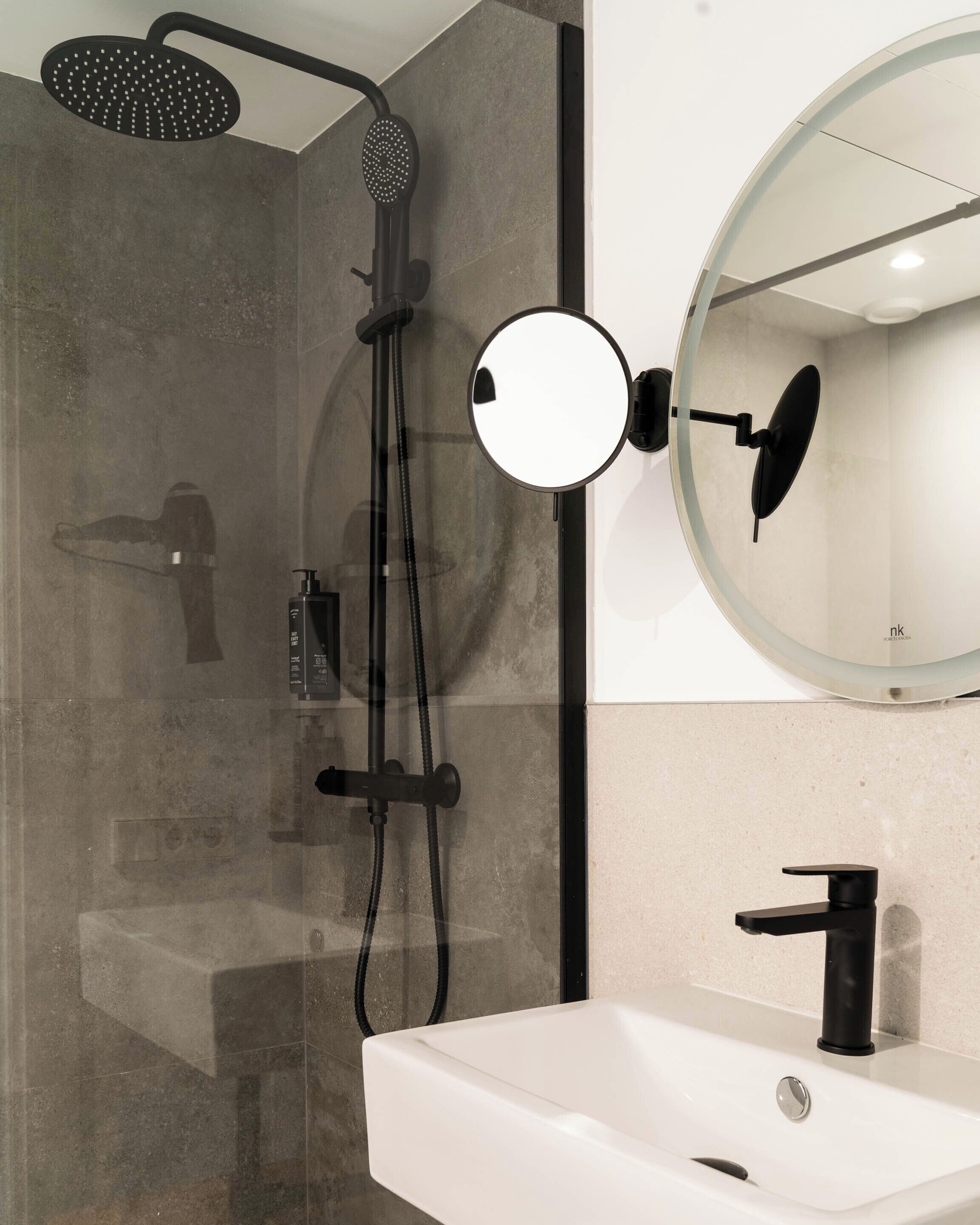 Un baño moderno con ducha envuelta en vidrio, un espejo redondo y un lavabo blanco.
