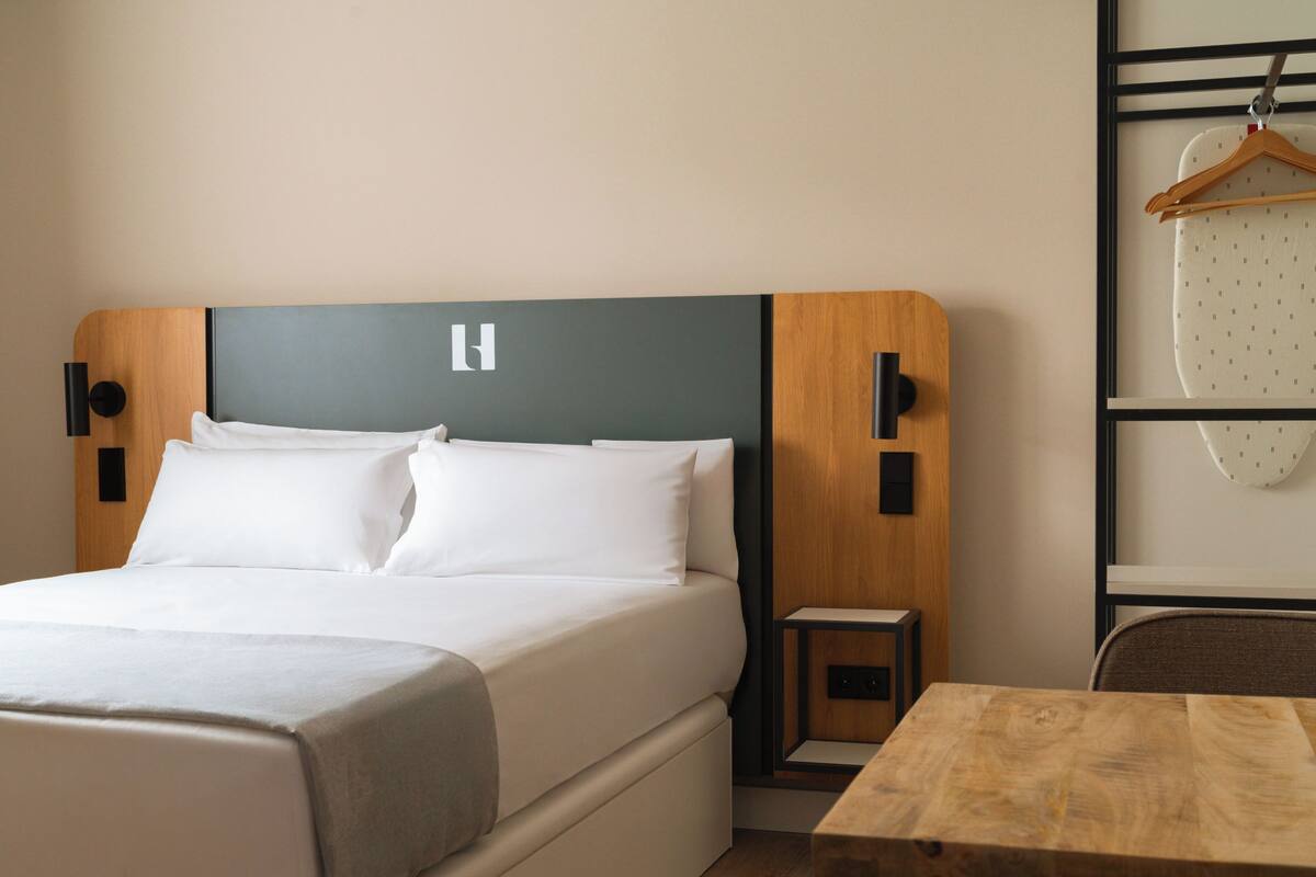A modern hotel room with a large bed, a wooden headboard, a small bedside table, and a wooden table.