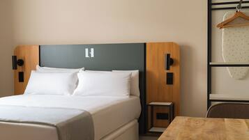 A modern hotel room with a large bed, a wooden headboard, a small bedside table, and a wooden table.