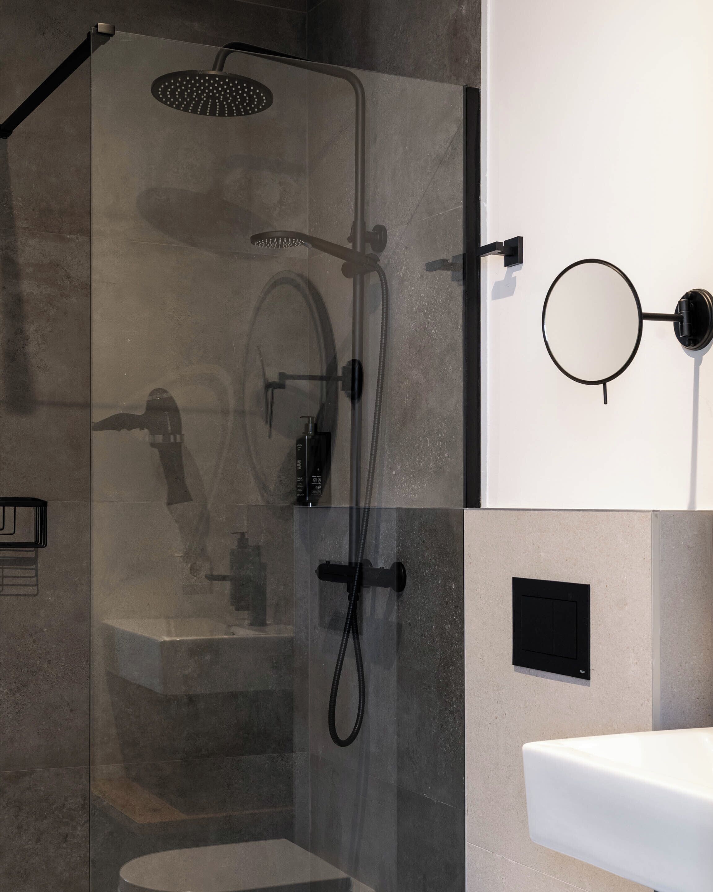 Un baño moderno con ducha envuelta en vidrio, inodoro de pared y un espejo redondo.