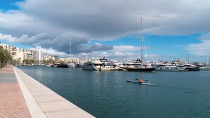 Un puerto deportivo con varios yates amarrados, una masa de agua tranquila y un paseo pavimentado a lo largo de la orilla.