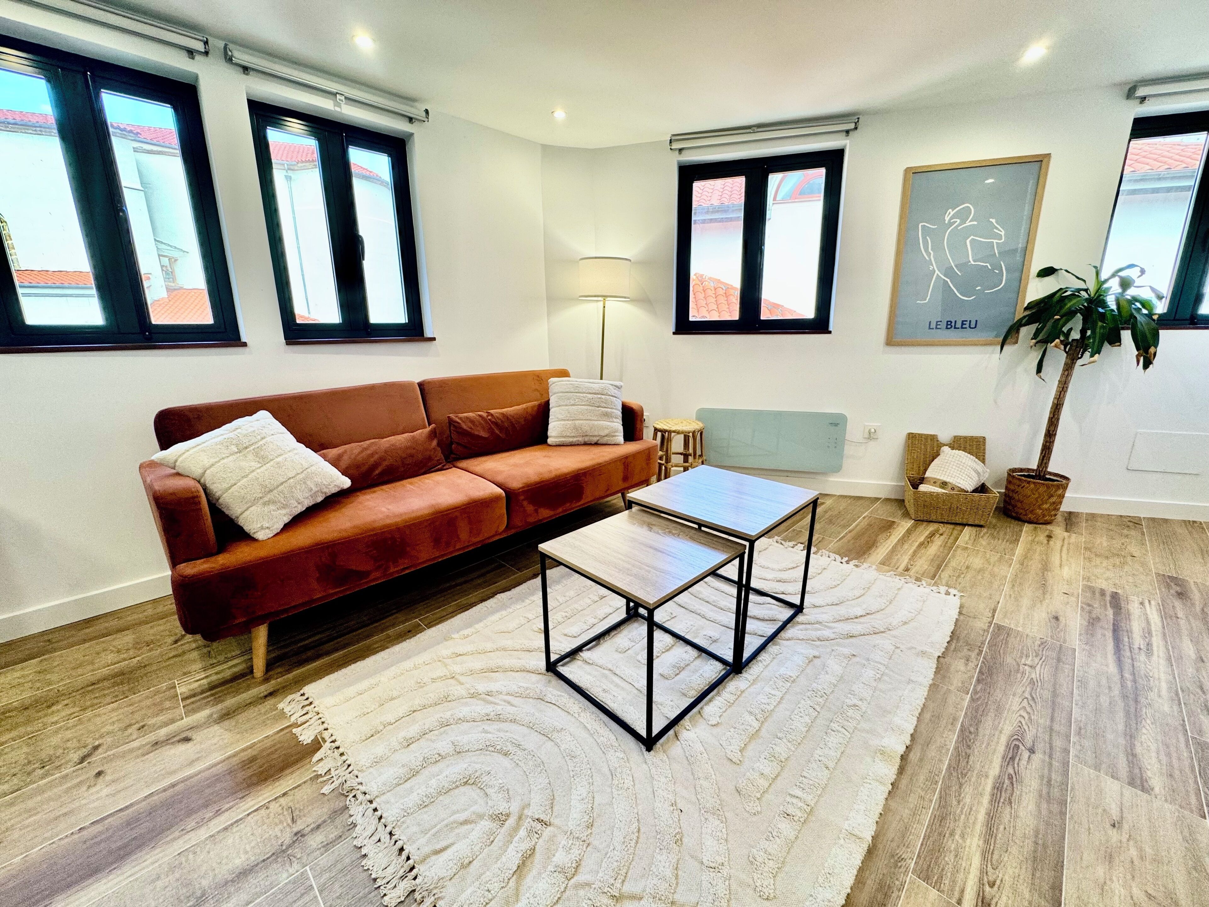 Een moderne woonkamer met een bruine bank, een bijzettafeltje, een lamp en een potplant.