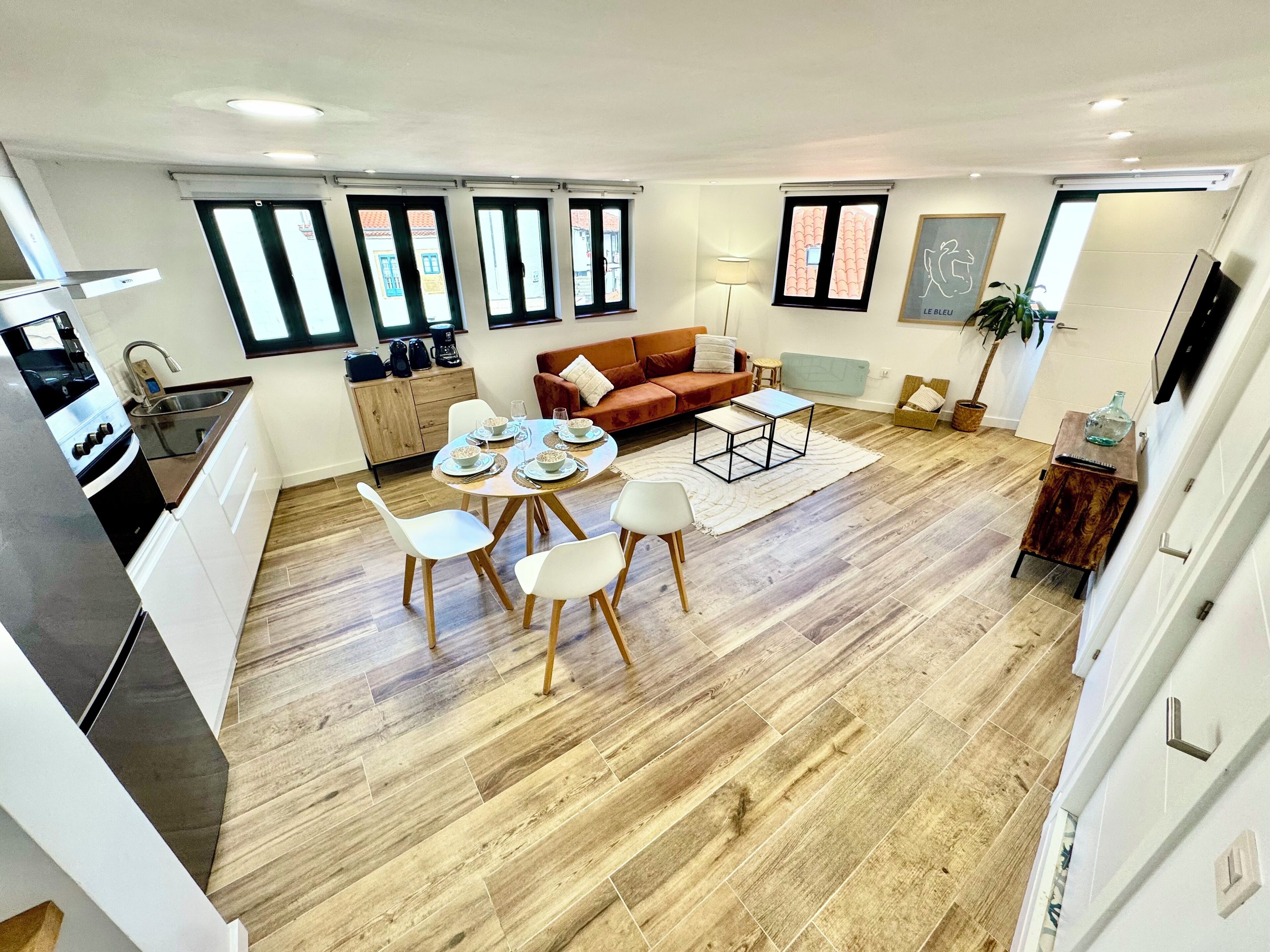A modern kitchen with a dining area, a sofa, and a TV.