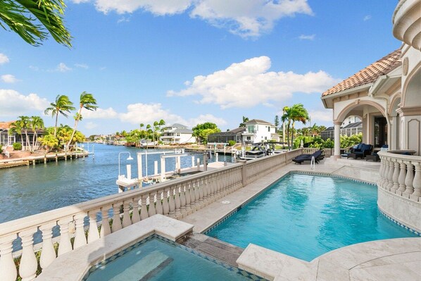 A swimming pool with a view of a marina, palm trees, and a building with a tiled roof.