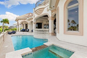 Ein luxuriöser Poolbereich mit geschwungenem Design, umgeben von einem weißen Gebäude mit Bogenfenstern und Balkonen.