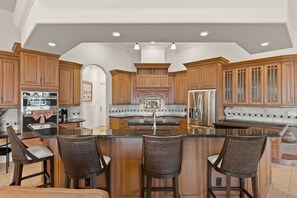 A spacious kitchen with wooden cabinets, a central island with bar stools, and stainless steel appliances.
