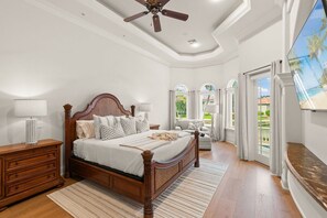 A bedroom with a wooden bed, a nightstand, a TV, and a view of the outdoors.