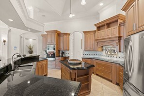 A spacious kitchen with wooden cabinets, a stainless steel refrigerator, and a granite countertop.