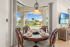 A dining area with a round table, chairs, and a view of a tropical landscape through a glass door. - Tigertail Luxury Beach Retreat -Heated Pool & Spa (Marco Island)