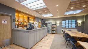 A bar area with a wooden counter, shelves of bottles, and a sign that reads "Eat Drink Enjoy". - Host Stay The Braunston Lodge (York)