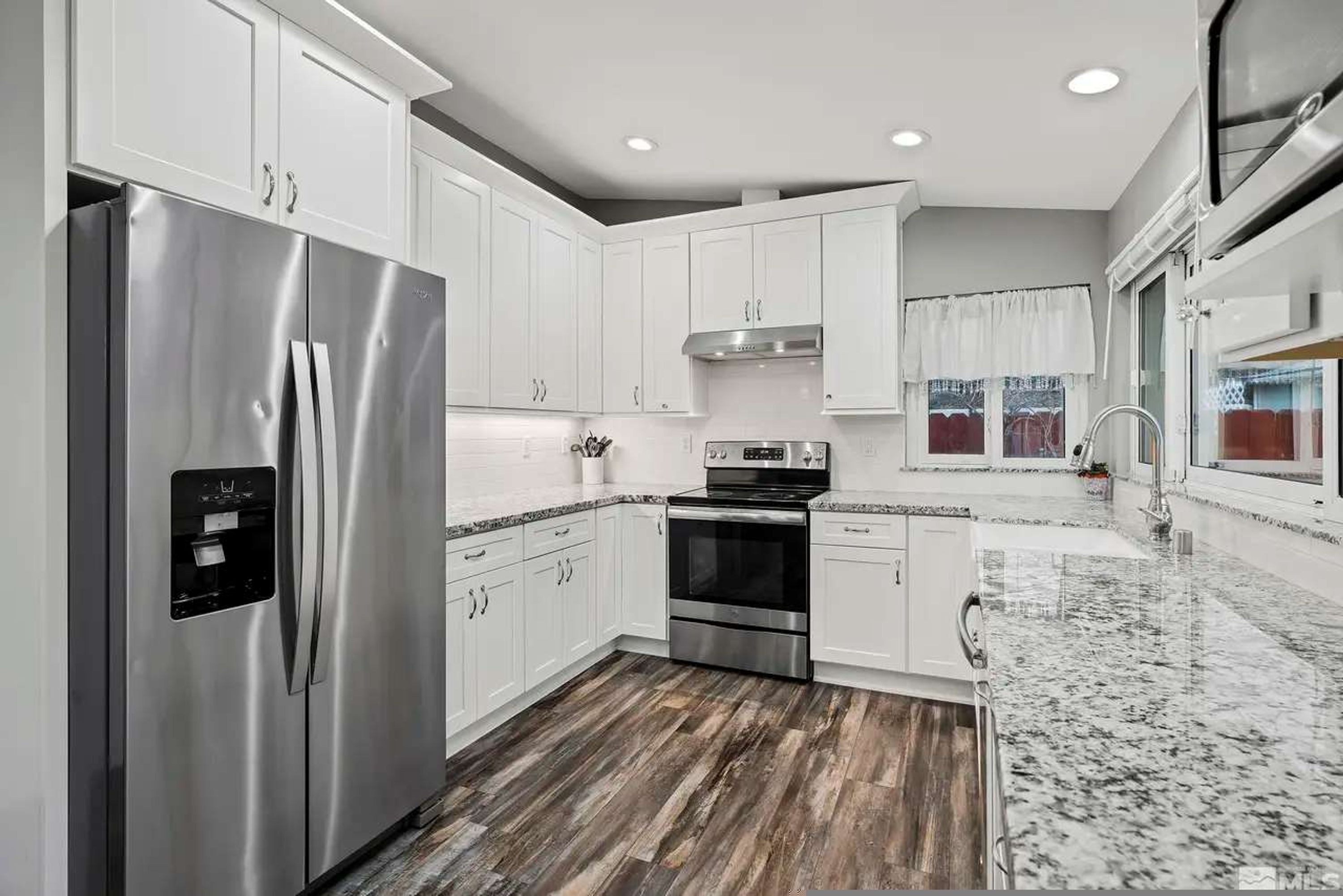 Una cocina moderna con armarios blancos, electrodomésticos de acero inoxidable y encimera de granito.